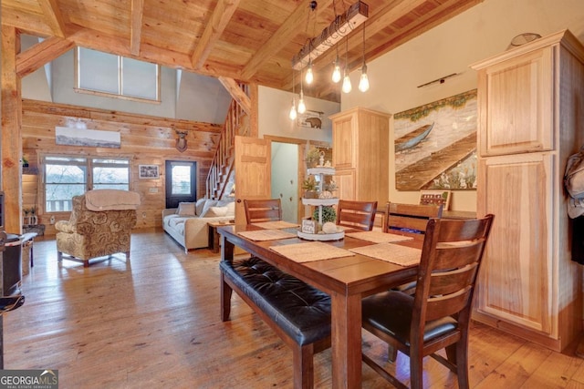 dining room featuring wood ceiling, light hardwood / wood-style flooring, beam ceiling, wooden walls, and a high ceiling