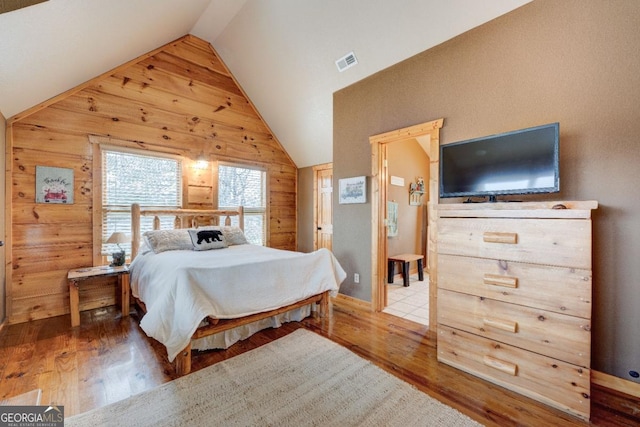 bedroom with wooden walls, vaulted ceiling, and hardwood / wood-style floors