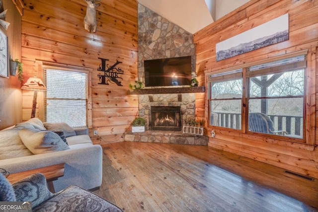 living room featuring wood walls, wood-type flooring, high vaulted ceiling, plenty of natural light, and a fireplace