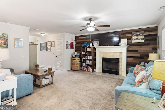 living room featuring wood walls, crown molding, ceiling fan, light colored carpet, and a fireplace