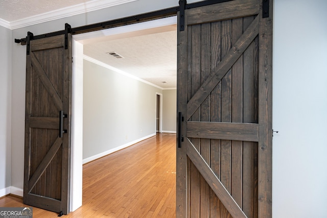 foyer entrance featuring crown molding, a barn door, a textured ceiling, and light wood-type flooring