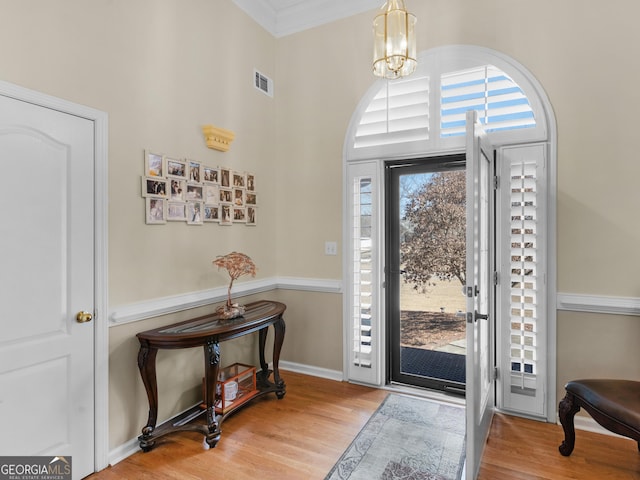 foyer featuring crown molding, hardwood / wood-style floors, and a notable chandelier