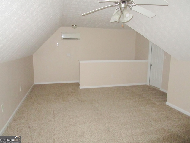 additional living space with lofted ceiling, light colored carpet, a textured ceiling, a wall unit AC, and ceiling fan