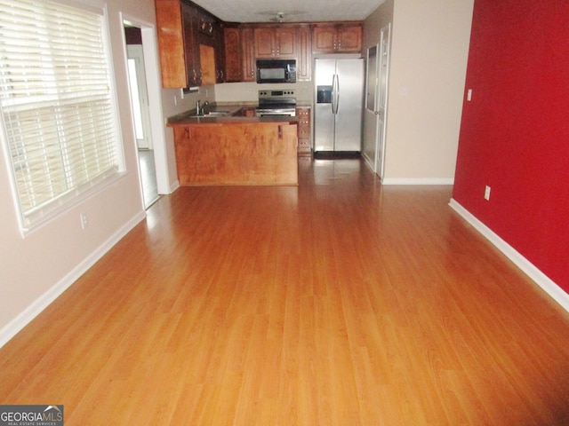 kitchen featuring sink, light wood-type flooring, kitchen peninsula, and appliances with stainless steel finishes