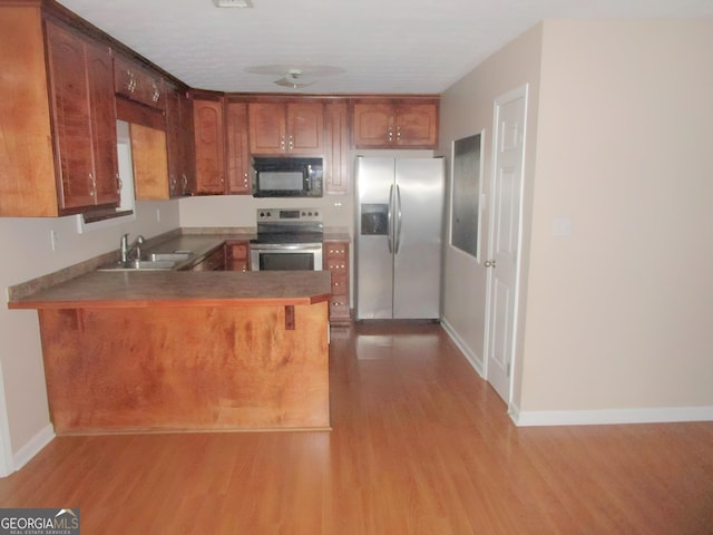 kitchen with appliances with stainless steel finishes, kitchen peninsula, sink, and light wood-type flooring