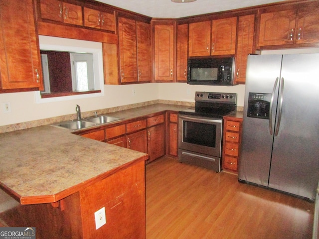 kitchen with appliances with stainless steel finishes, sink, light hardwood / wood-style flooring, and kitchen peninsula