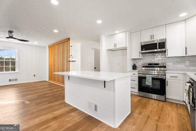 kitchen with a kitchen bar, white cabinetry, tasteful backsplash, light hardwood / wood-style flooring, and stainless steel appliances