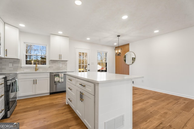 kitchen with appliances with stainless steel finishes, pendant lighting, white cabinets, decorative backsplash, and a center island