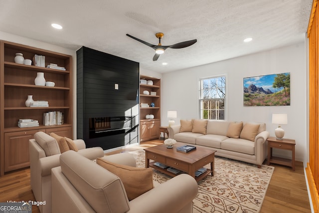 living room featuring ceiling fan, a large fireplace, light hardwood / wood-style floors, and a textured ceiling