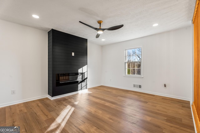 unfurnished living room featuring ceiling fan, hardwood / wood-style flooring, a fireplace, and a textured ceiling