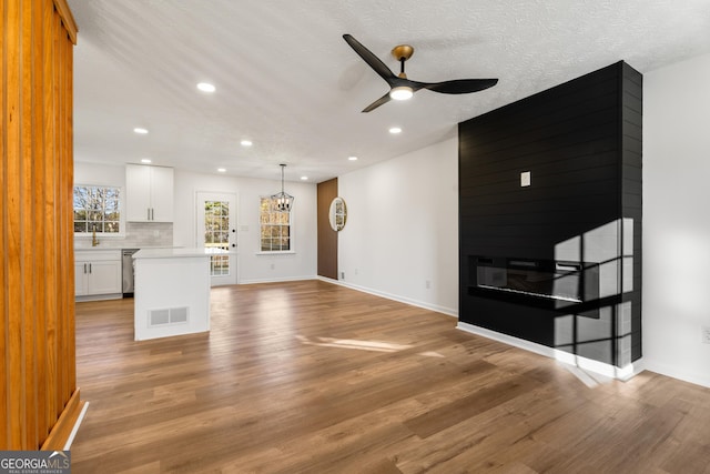 unfurnished living room with ceiling fan, a large fireplace, light hardwood / wood-style flooring, and a textured ceiling