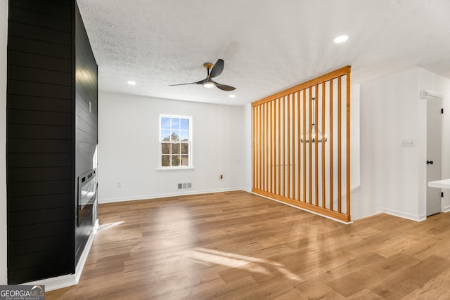 unfurnished living room with ceiling fan, a textured ceiling, a fireplace, and light hardwood / wood-style flooring