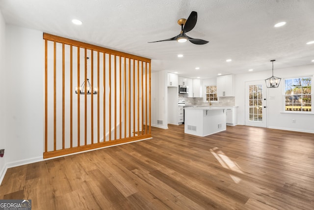 unfurnished living room featuring dark hardwood / wood-style floors, ceiling fan with notable chandelier, and a textured ceiling