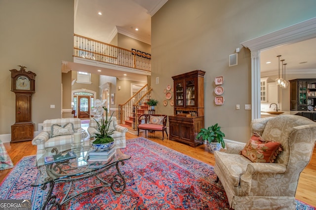 living room featuring sink, a towering ceiling, ornamental molding, and light hardwood / wood-style floors