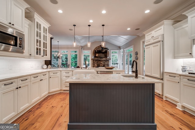 kitchen with sink, light stone counters, a center island with sink, stainless steel microwave, and pendant lighting