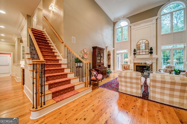 living room featuring crown molding, a premium fireplace, light hardwood / wood-style flooring, and a high ceiling