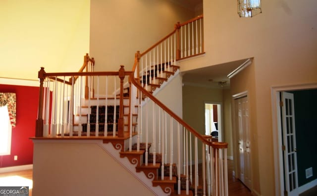 stairs featuring crown molding, a towering ceiling, and baseboards