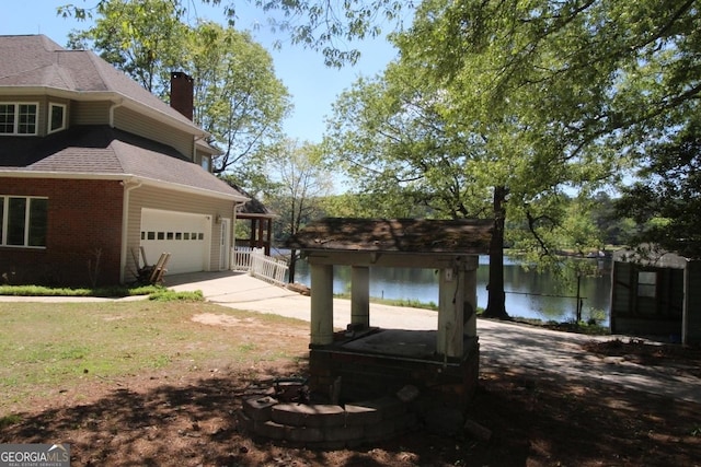 view of side of home featuring driveway, a chimney, roof with shingles, a water view, and brick siding