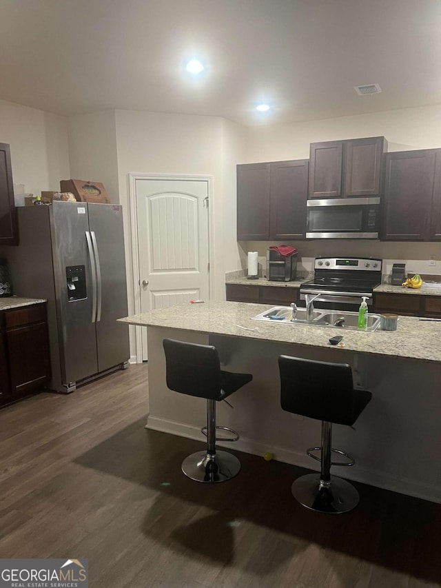 kitchen with dark hardwood / wood-style floors, dark brown cabinets, stainless steel appliances, and a kitchen breakfast bar