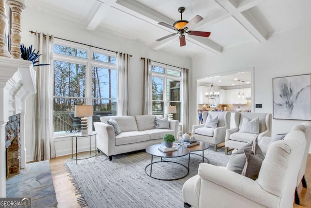 living room featuring ceiling fan with notable chandelier, beam ceiling, coffered ceiling, a stone fireplace, and light wood-type flooring