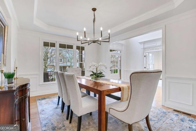 dining room featuring ornamental molding, light hardwood / wood-style flooring, an inviting chandelier, and a tray ceiling