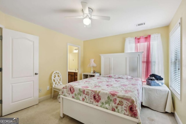 bedroom featuring multiple windows, light carpet, ceiling fan, and ensuite bathroom