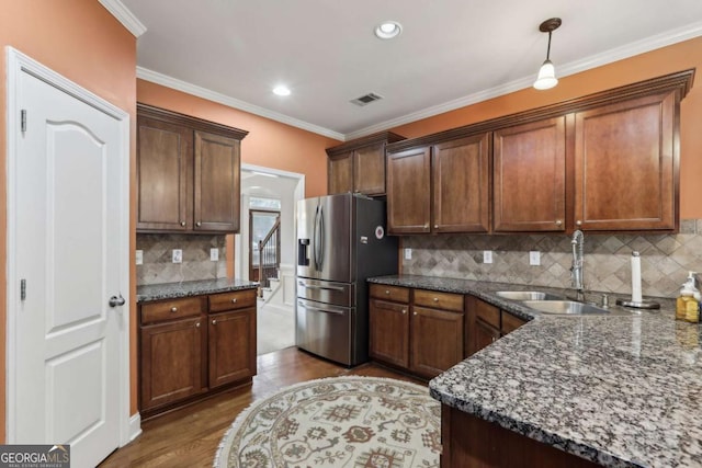 kitchen featuring sink, hanging light fixtures, stainless steel fridge, dark stone counters, and hardwood / wood-style floors