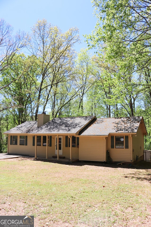 view of front facade with a chimney, a shingled roof, and a front lawn