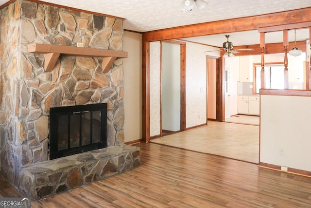 unfurnished living room featuring hardwood / wood-style flooring, a stone fireplace, a textured ceiling, and crown molding