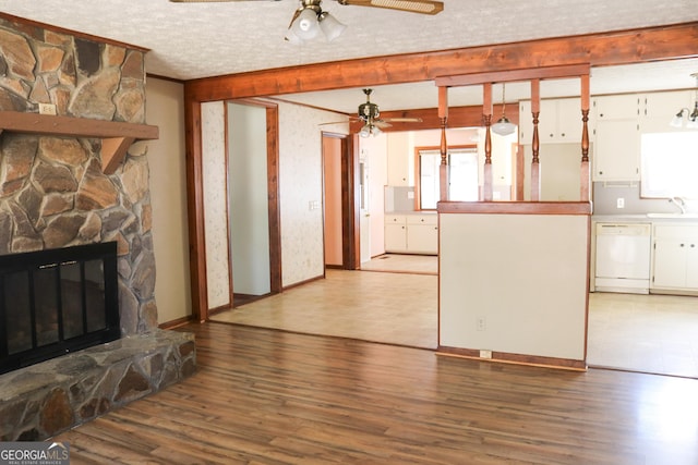 unfurnished living room featuring a ceiling fan, a stone fireplace, a sink, and wood finished floors