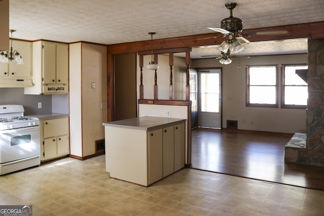 kitchen featuring a textured ceiling, white gas range, kitchen peninsula, pendant lighting, and cream cabinets