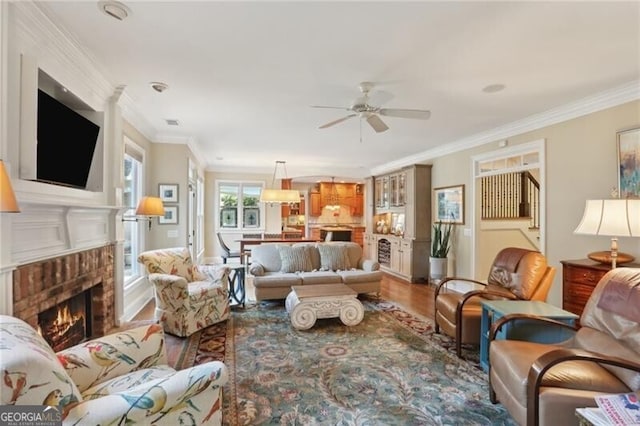 living room featuring wood-type flooring, ceiling fan, a fireplace, and crown molding