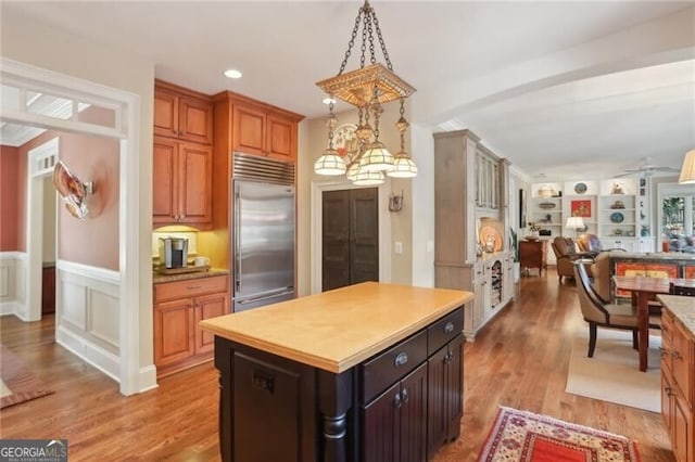 kitchen with built in fridge, a kitchen island, beam ceiling, dark brown cabinetry, and light wood-type flooring