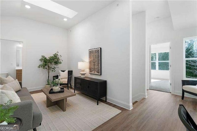 living room featuring a skylight, high vaulted ceiling, and light hardwood / wood-style floors