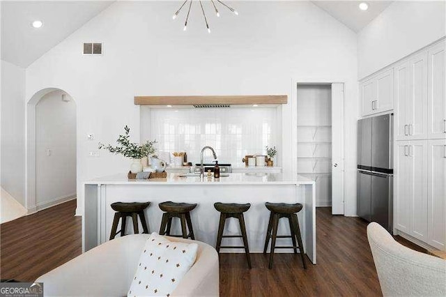 kitchen with sink, stainless steel refrigerator, white cabinetry, dark hardwood / wood-style floors, and a kitchen bar