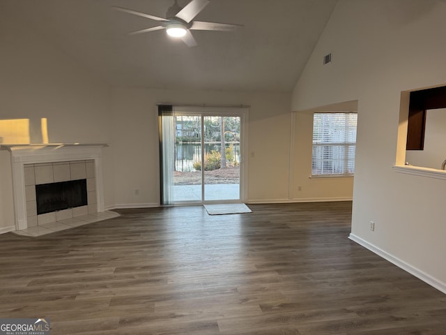 unfurnished living room with high vaulted ceiling, dark wood-type flooring, a tile fireplace, and ceiling fan