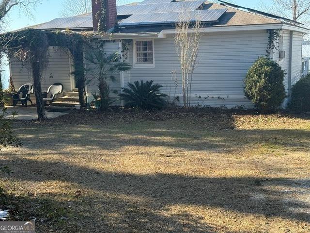 view of home's exterior with solar panels, a patio, a lawn, and a chimney