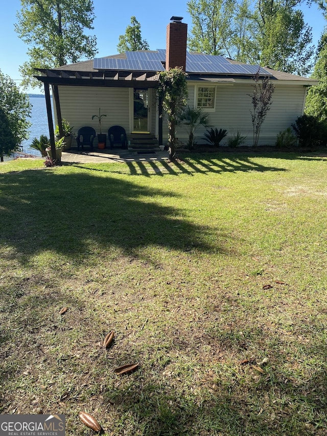 back of house with a patio, entry steps, a lawn, roof mounted solar panels, and metal roof