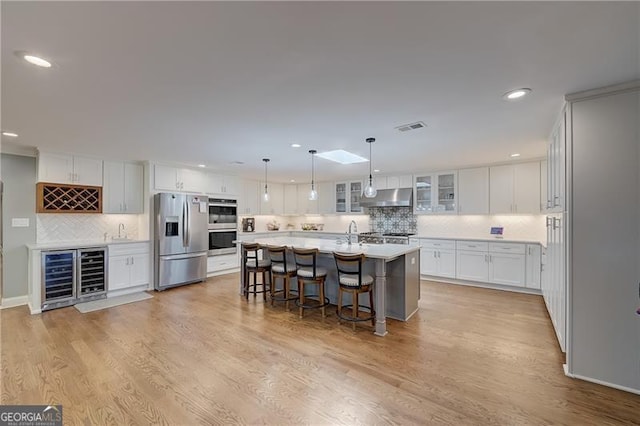 kitchen with white cabinetry, an island with sink, beverage cooler, a kitchen bar, and stainless steel appliances