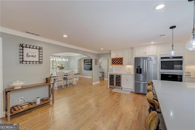 kitchen with wine cooler, white cabinetry, crown molding, appliances with stainless steel finishes, and pendant lighting