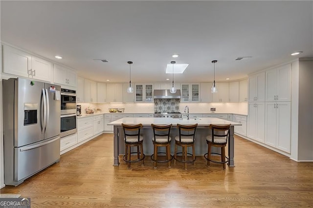 kitchen with white cabinetry, appliances with stainless steel finishes, a breakfast bar, and a center island with sink