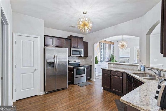 kitchen with sink, appliances with stainless steel finishes, a notable chandelier, pendant lighting, and light stone countertops