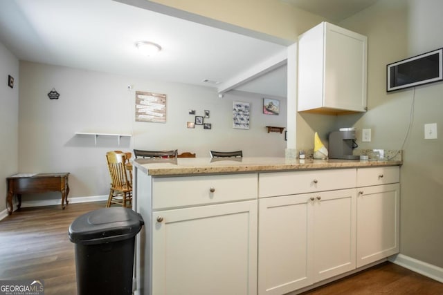 kitchen featuring dark wood-type flooring, kitchen peninsula, light stone countertops, and white cabinets