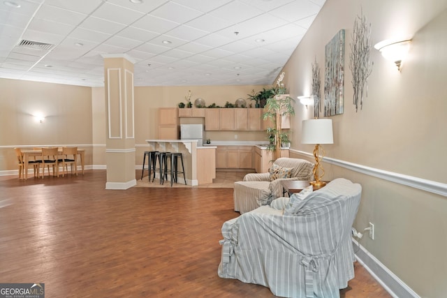 living area with decorative columns, wood-type flooring, and a paneled ceiling