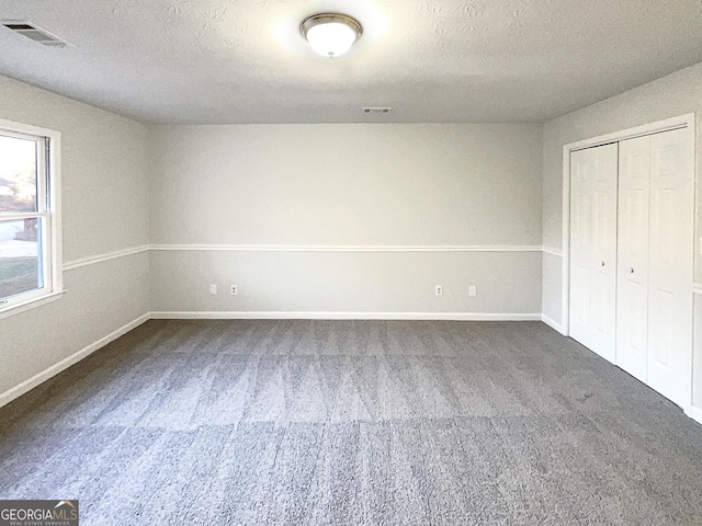 unfurnished bedroom with a closet, a textured ceiling, and dark colored carpet