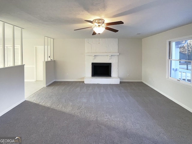 unfurnished living room with ceiling fan, a large fireplace, dark carpet, and a textured ceiling