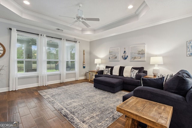 living room featuring dark hardwood / wood-style floors, ceiling fan, ornamental molding, and a tray ceiling