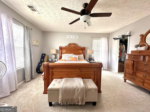 bedroom with multiple windows, a walk in closet, light carpet, and ceiling fan