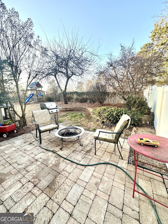 view of patio with a grill, a playground, and an outdoor fire pit