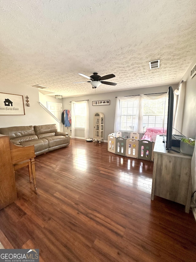 living room with a textured ceiling, dark wood-type flooring, and ceiling fan